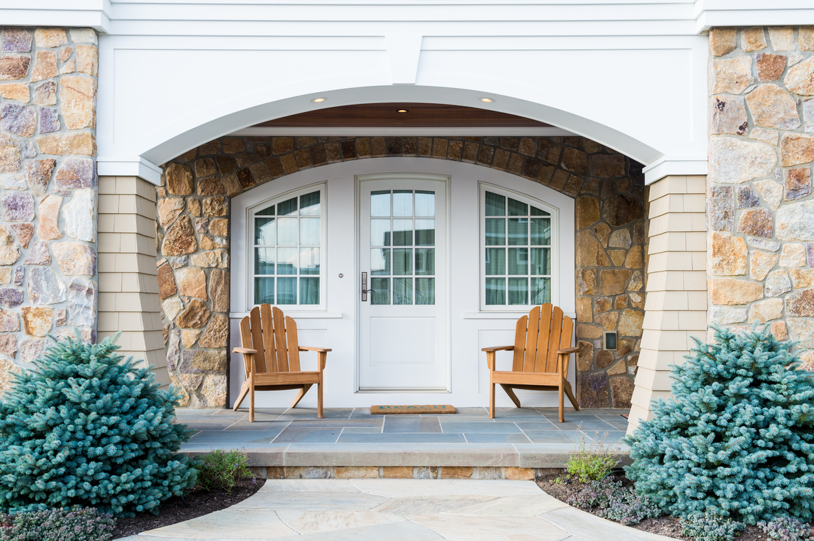 There are two chairs on the porch of a house.
