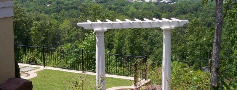 A white pergola is sitting on top of a lush green hillside.