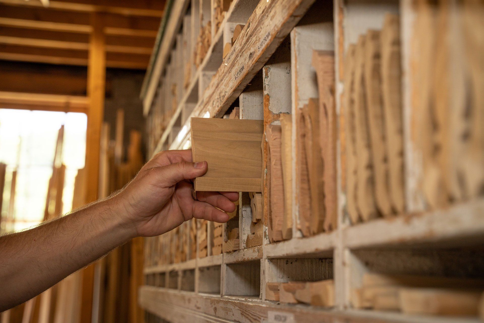 A person is taking a piece of wood from a shelf in a woodworking shop.