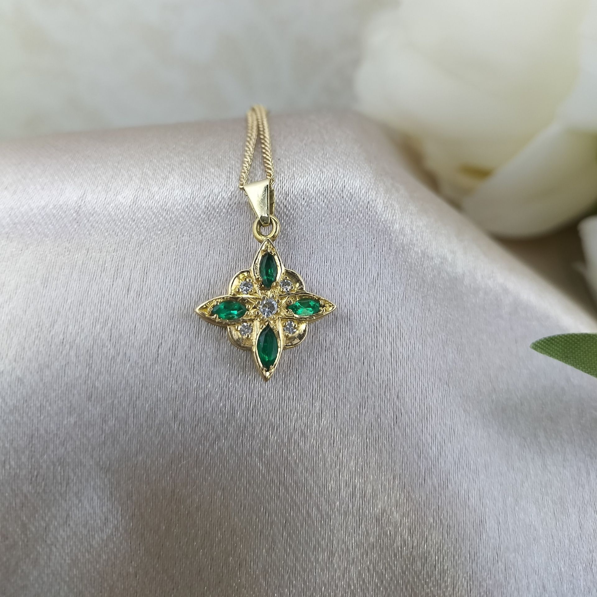 A gold necklace with emeralds and diamonds is sitting on a white cloth.