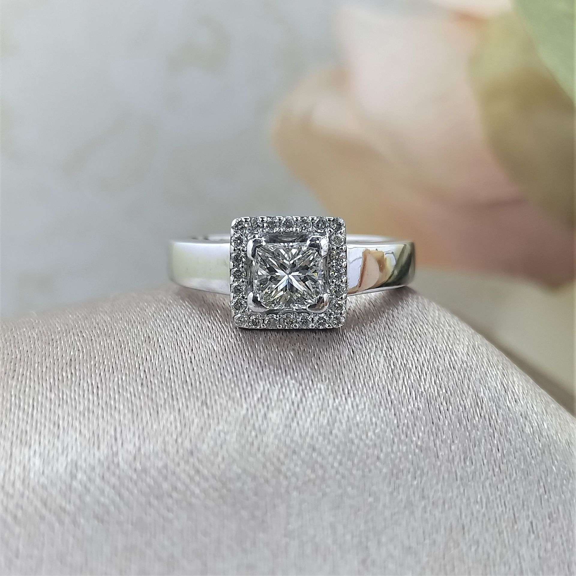 A white gold ring with a square diamond in the center is sitting on a cloth.