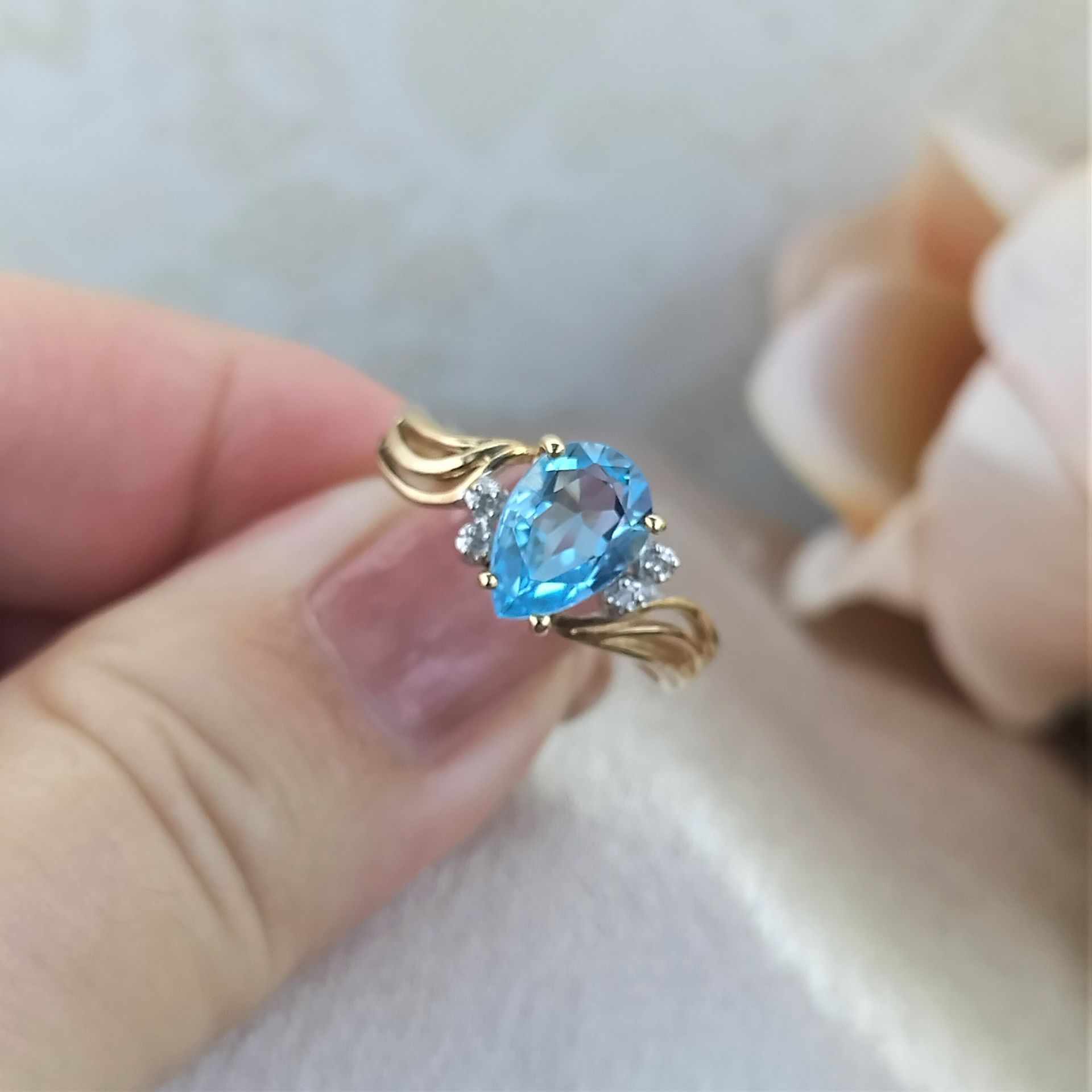 A person is holding a gold ring with a blue stone in the center