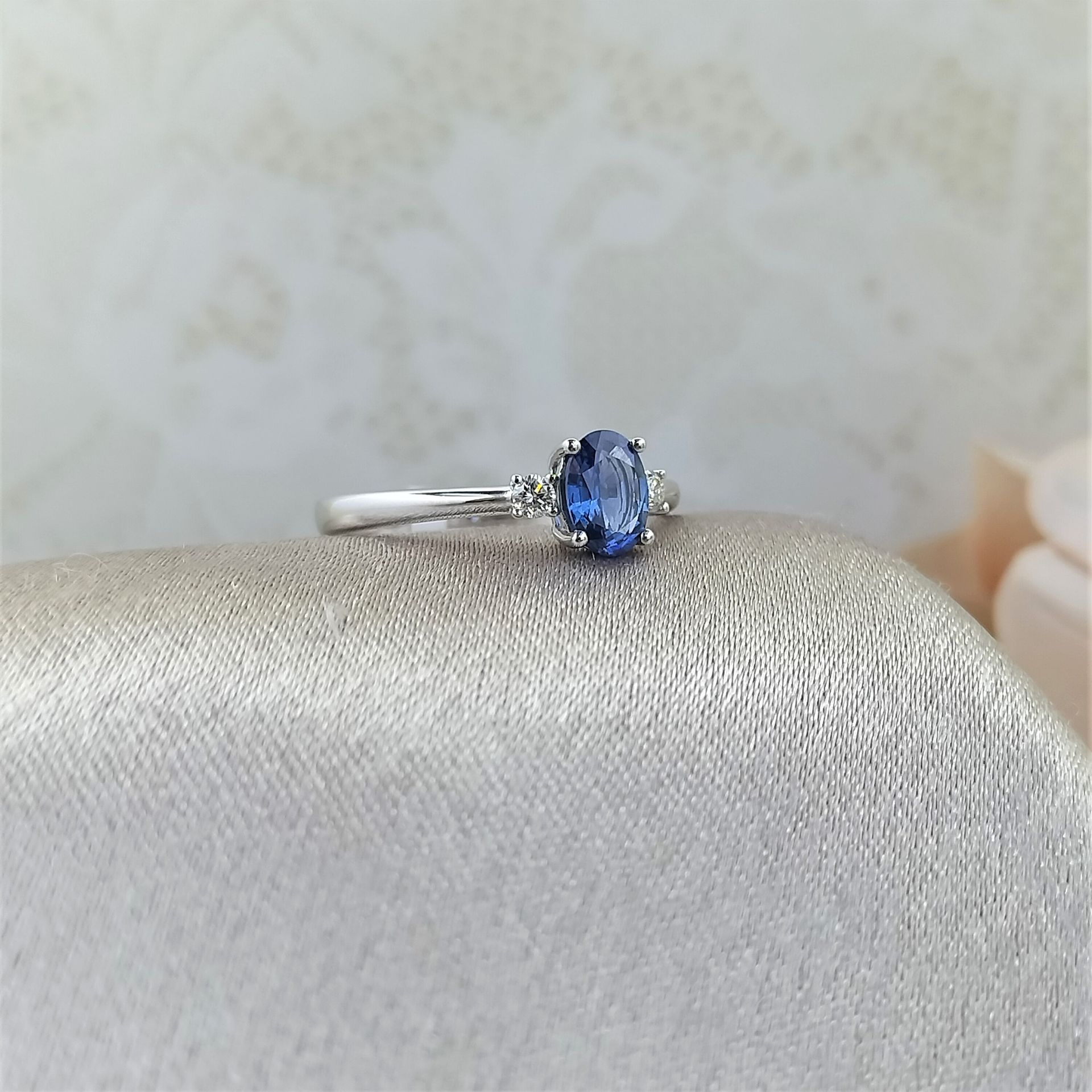 A sapphire and diamond ring is sitting on a white cloth.