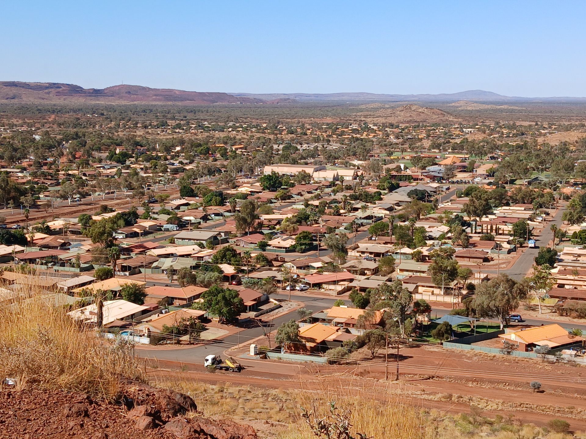 Aerial view of a town with red-roofed houses and sparse trees under a blue sky.