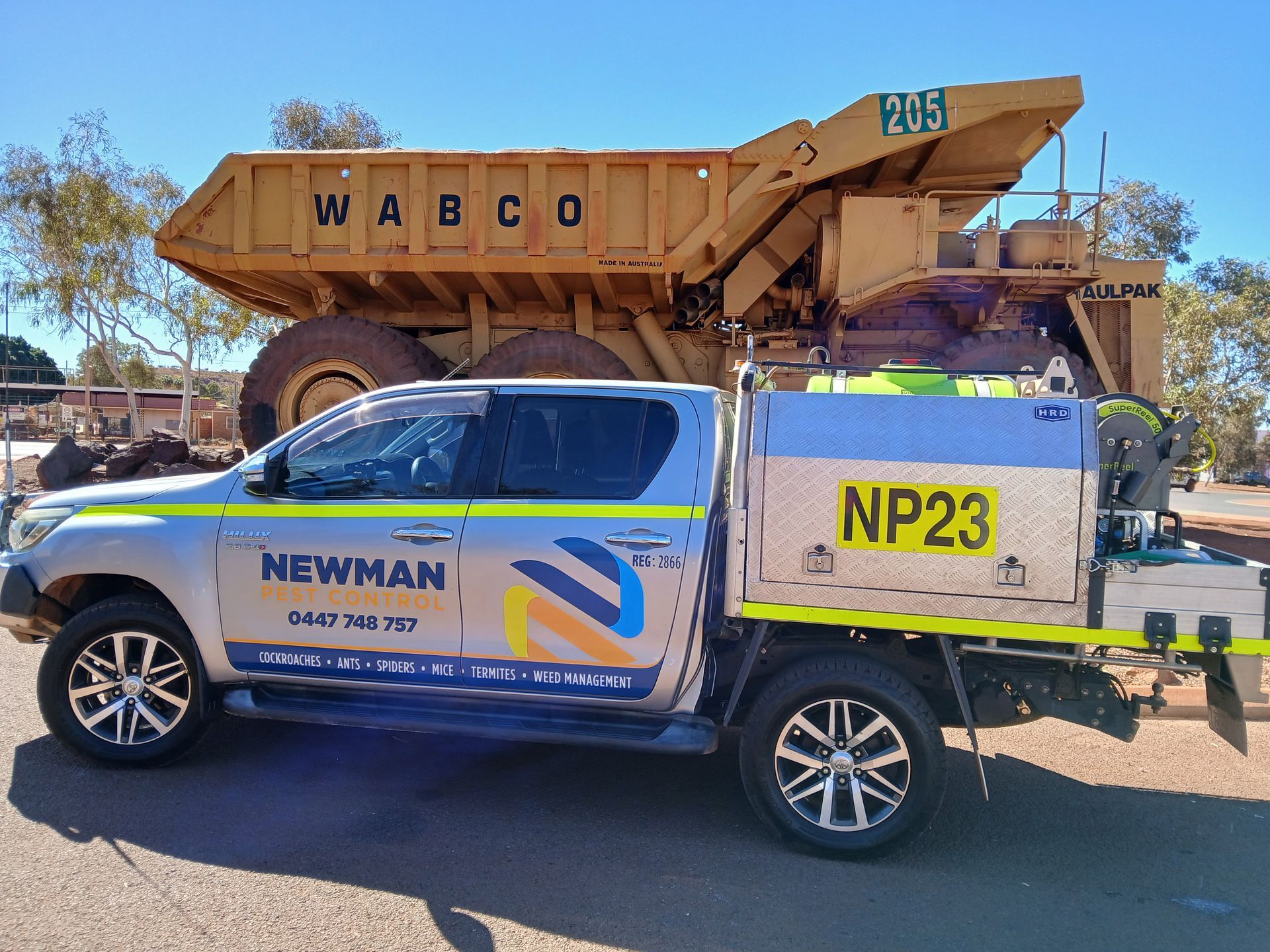 A Newman service truck, parked beside a large yellow mining dump truck, in an outdoor setting.