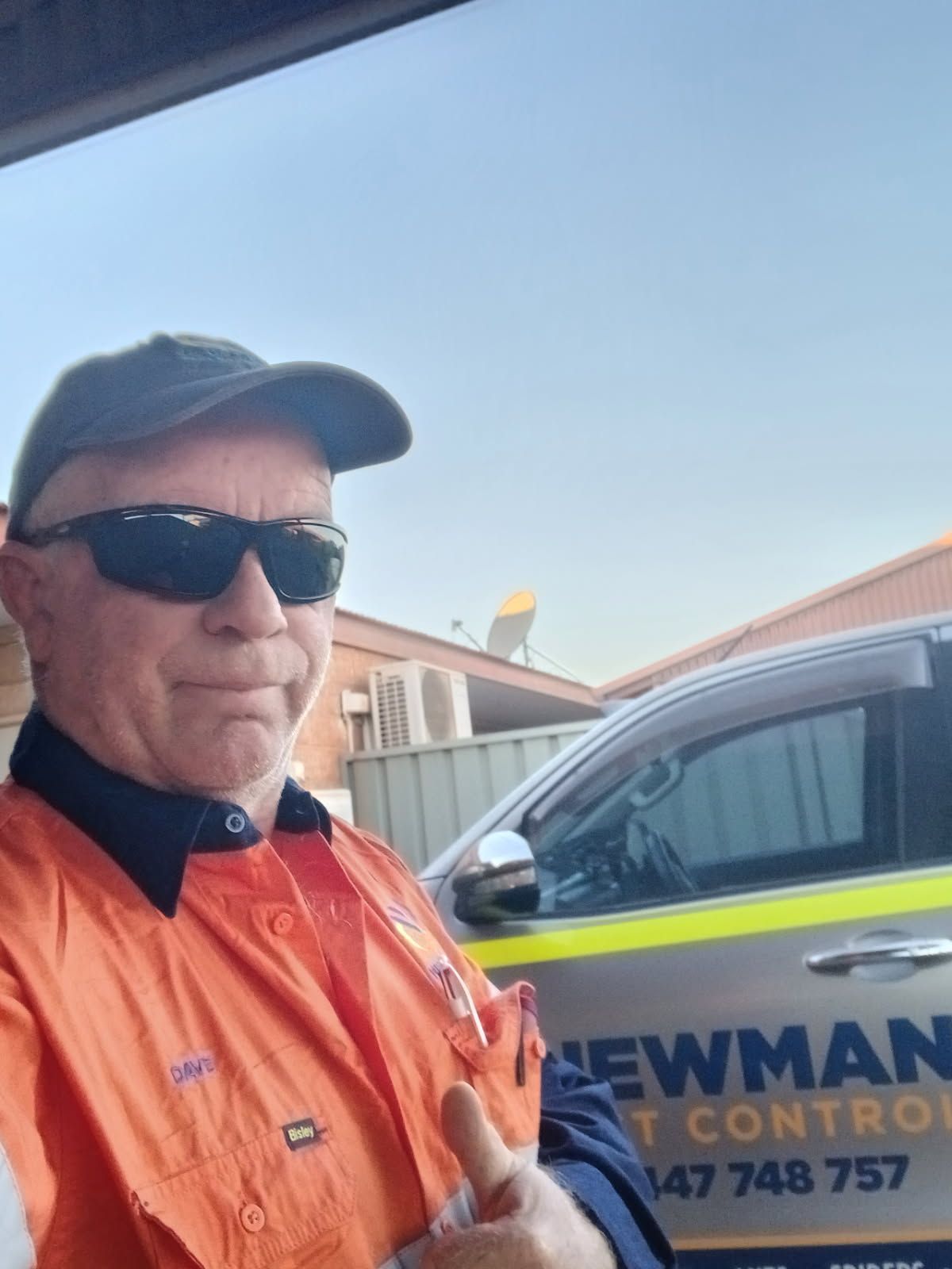 Man in work clothes and sunglasses gives a thumbs up. Beside a company truck.