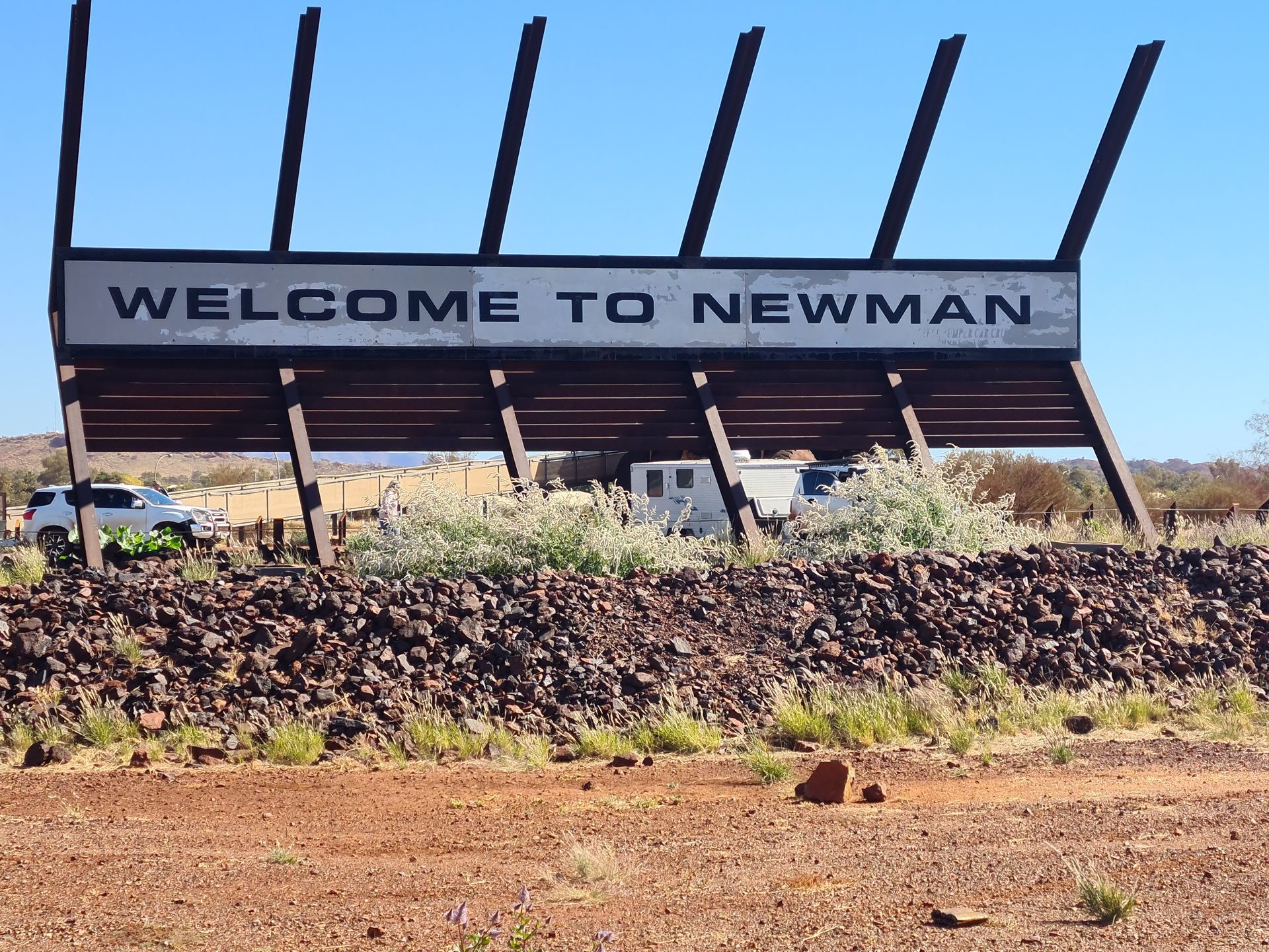 Welcome sign for Newman, Australia, with a brown rock border, and a blue sky.