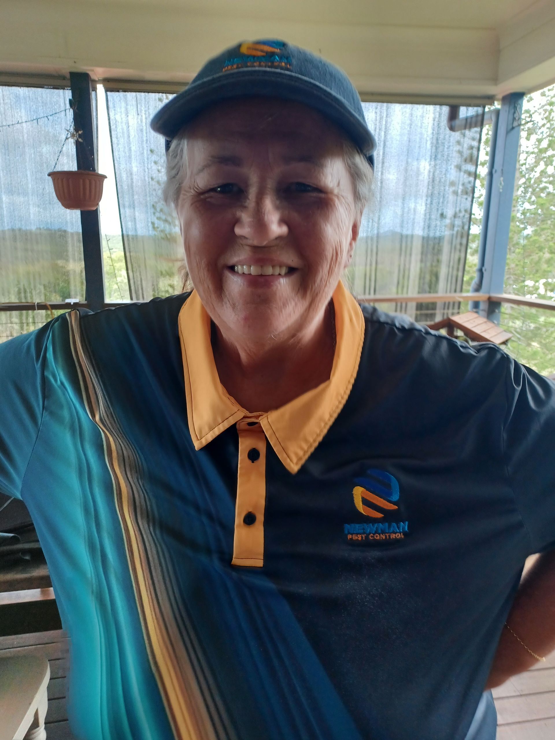 Woman in blue and gold shirt and cap smiles on a porch.
