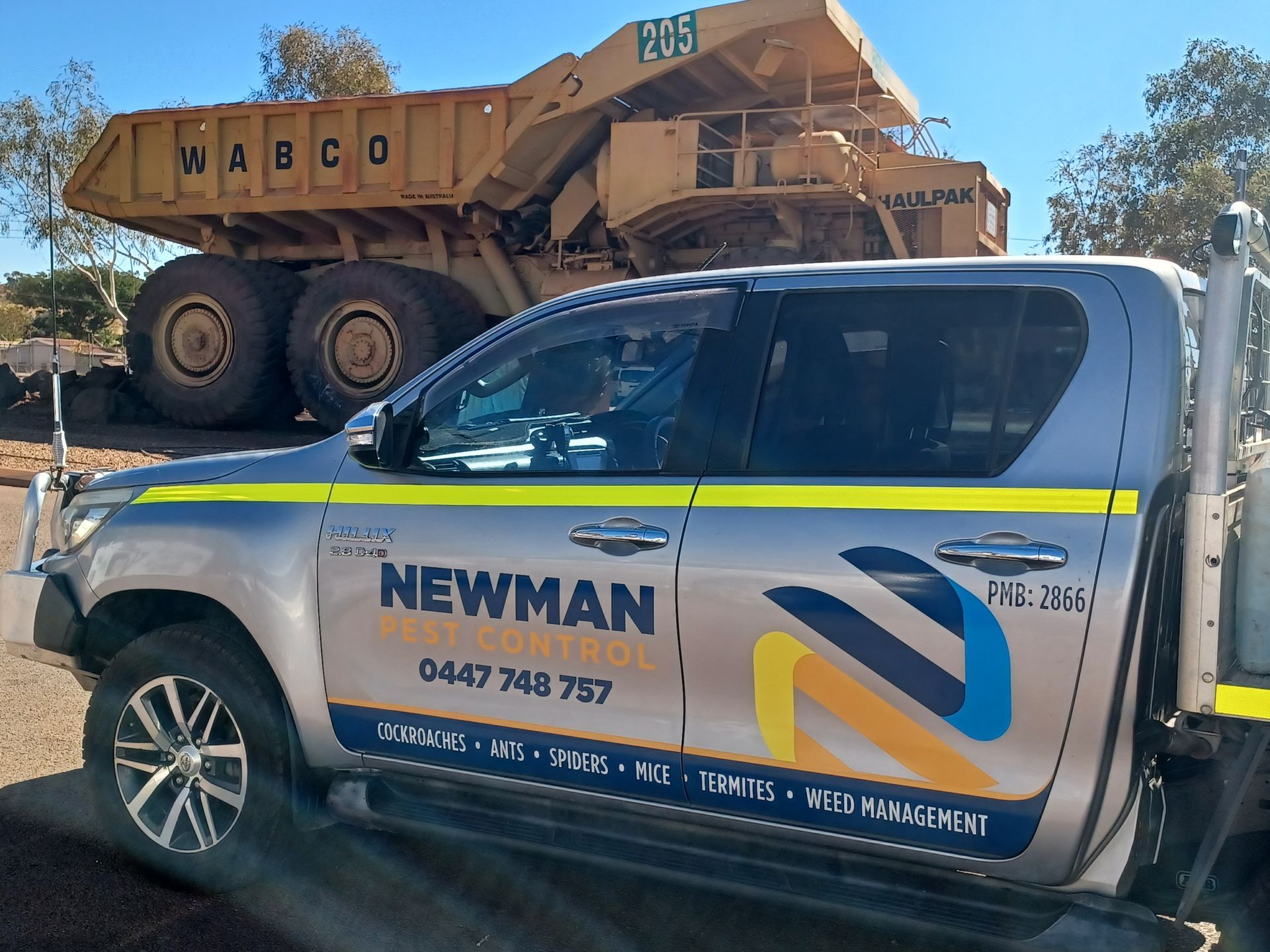 Silver Newman transport truck beside a large yellow WASCO mining truck outdoors.