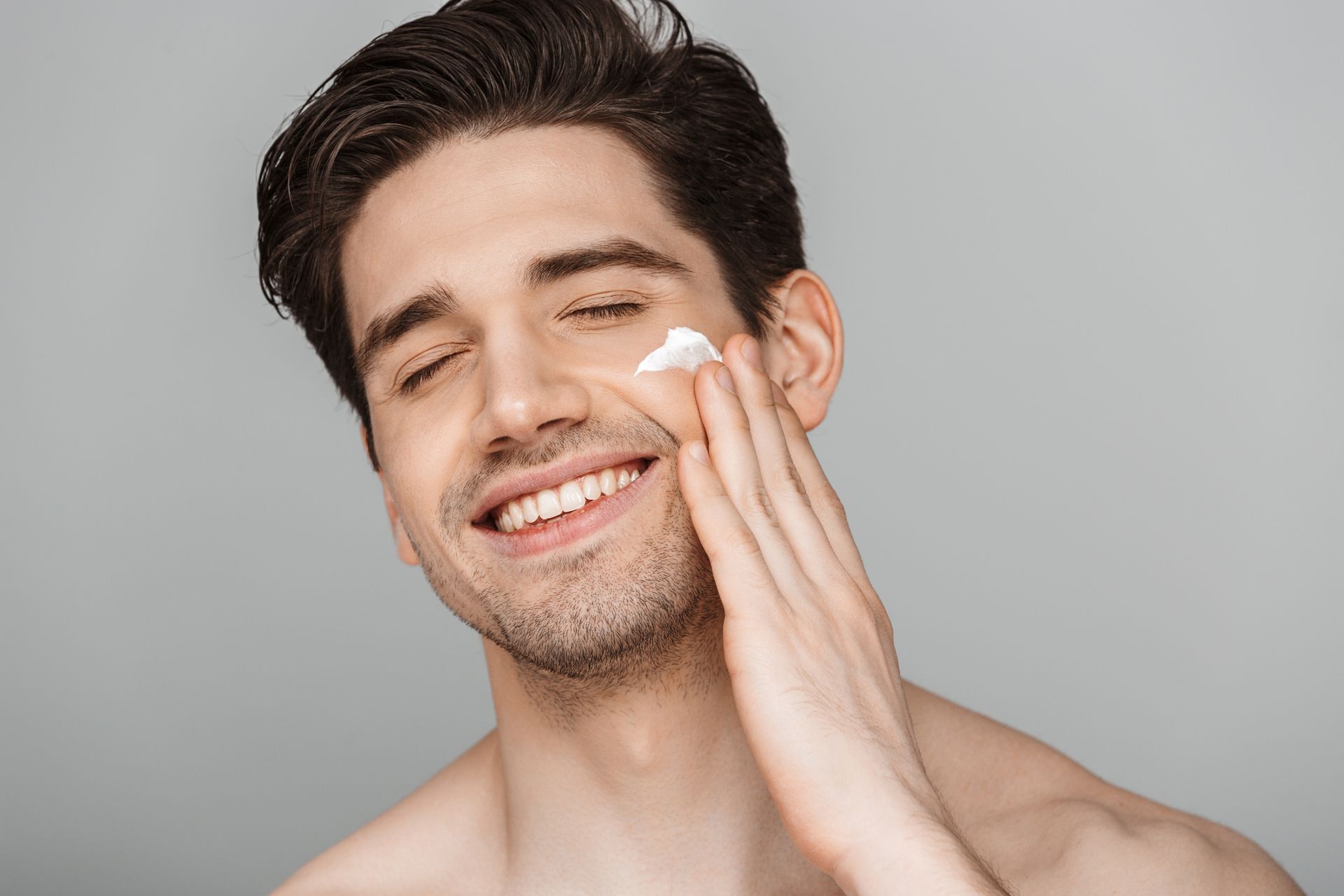 a man is smiling while applying cream to his face .