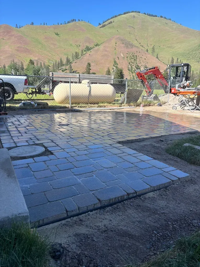 Newly laid brick patio with mountain backdrop; construction equipment visible.
