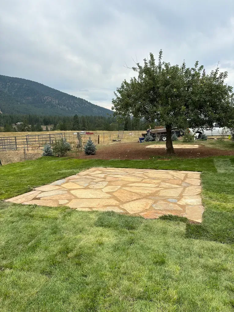 Stone patio with grass border, tree, and mountain backdrop on a cloudy day.