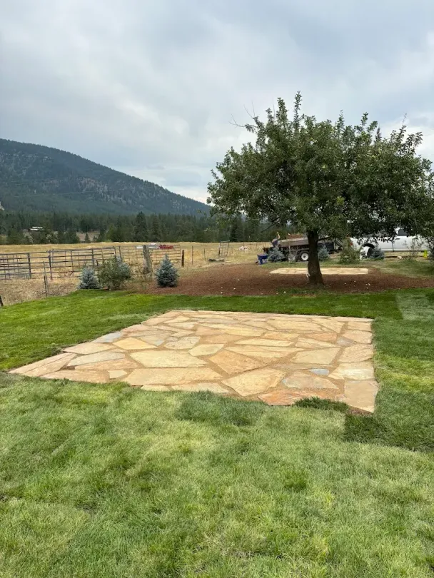 Flagstone pathway under construction; tractor bucket holds material; brown and tan colors.