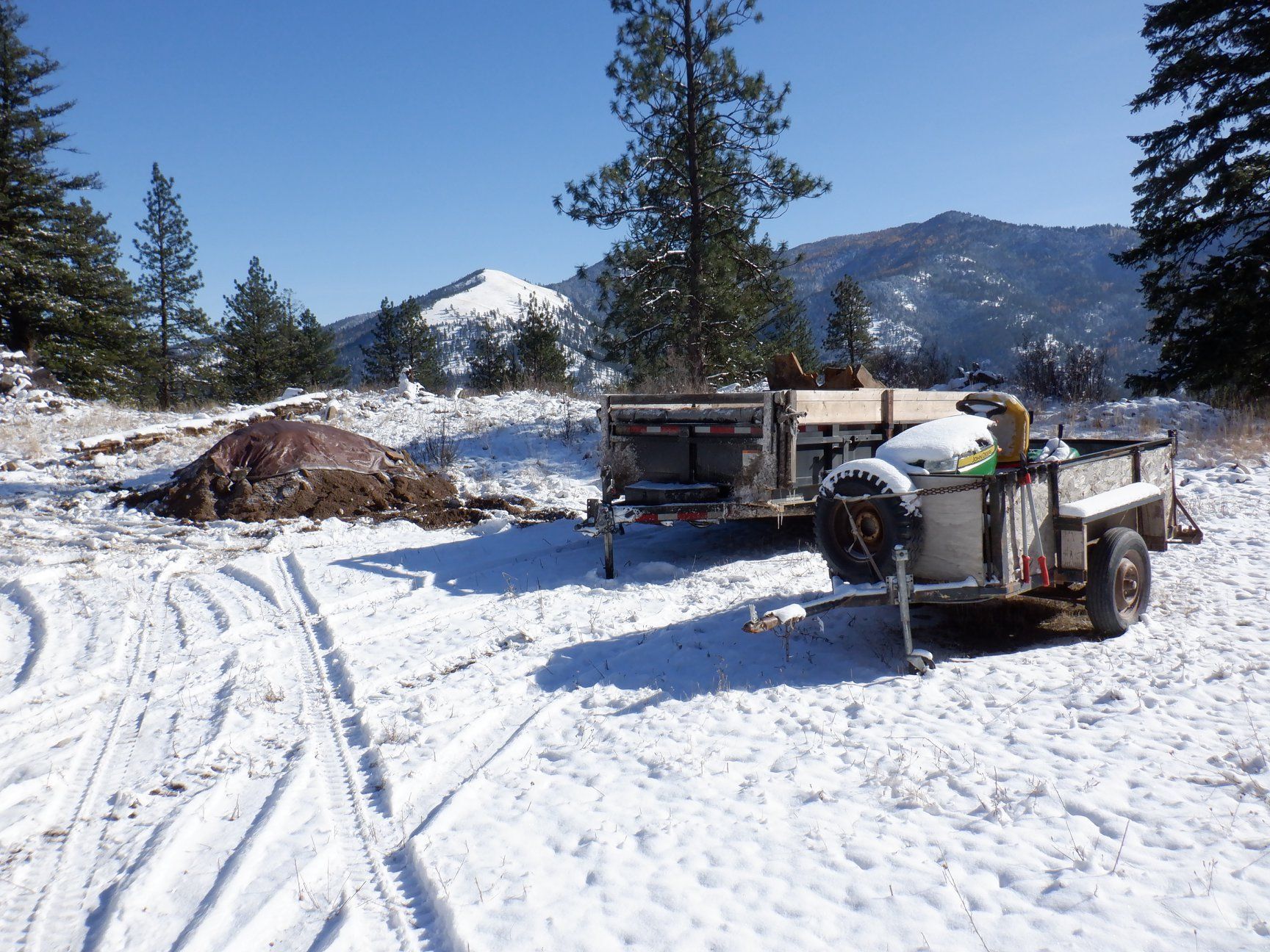 Snowy scene with two trailers in a clearing, mountain backdrop.