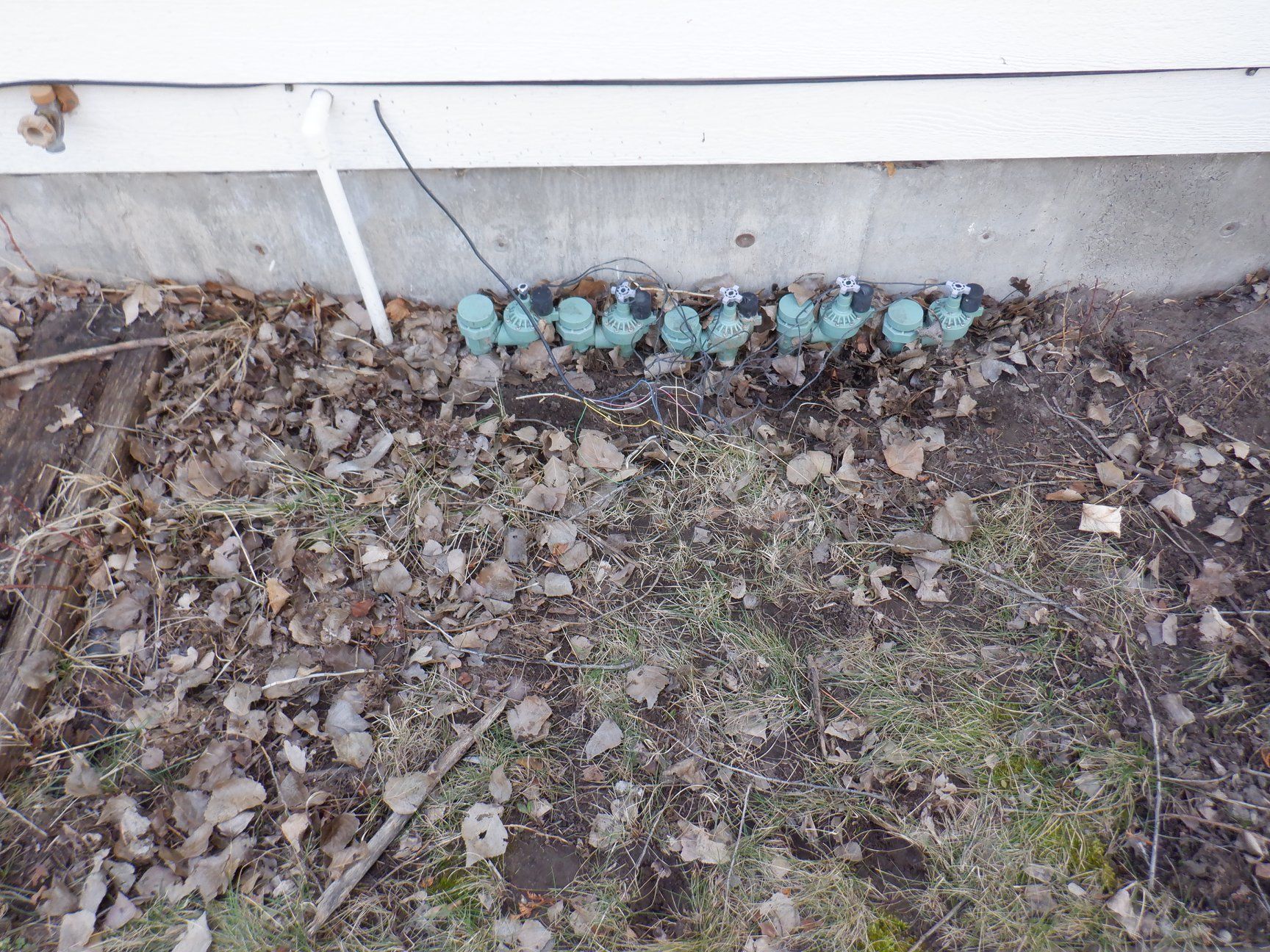 Row of blue glass insulators along a concrete foundation. Ground covered with leaves and grass.