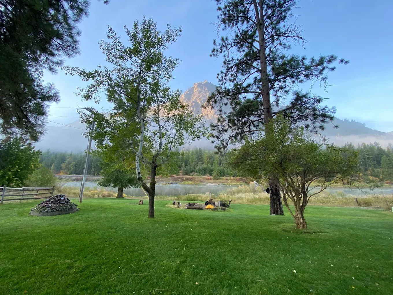 Green lawn with trees, fire pit, and misty mountain in background.