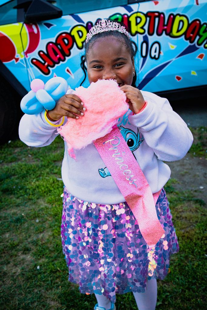 Girl in a tiara and sequin skirt smiles, holding a pink sash that says