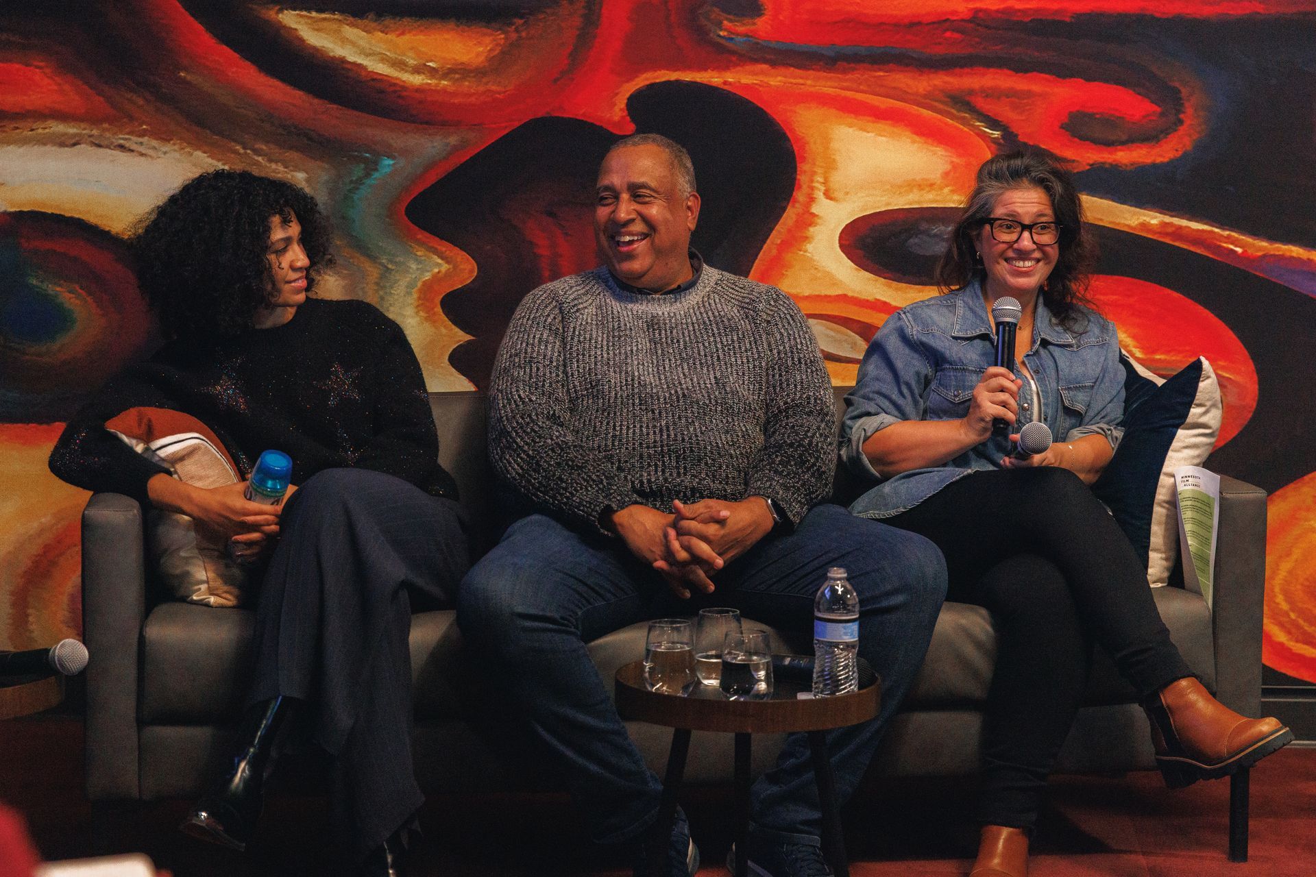 Two women are sitting in front of a television talking to a group of people.