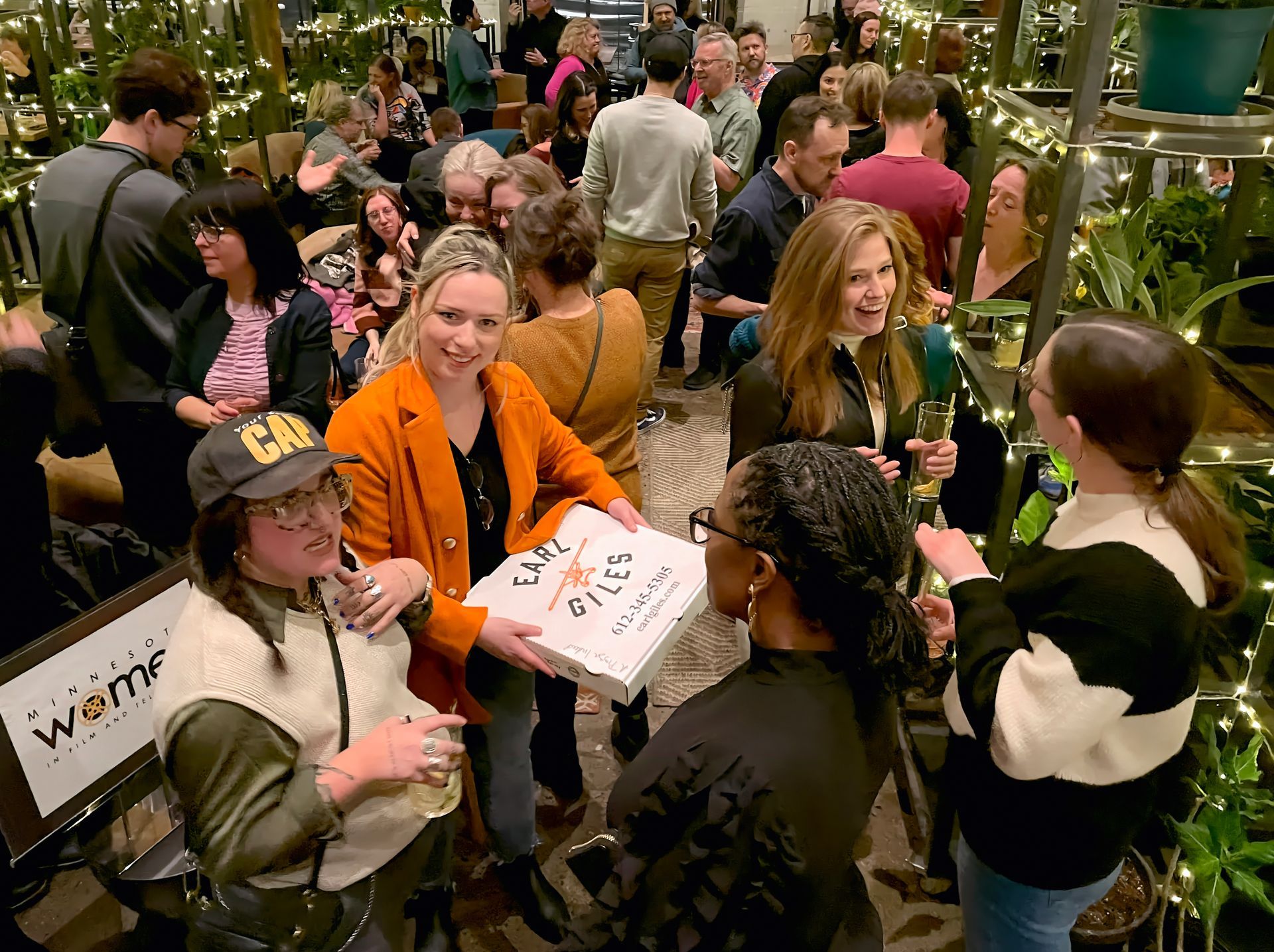 A group of people are standing around a table holding a pizza box.