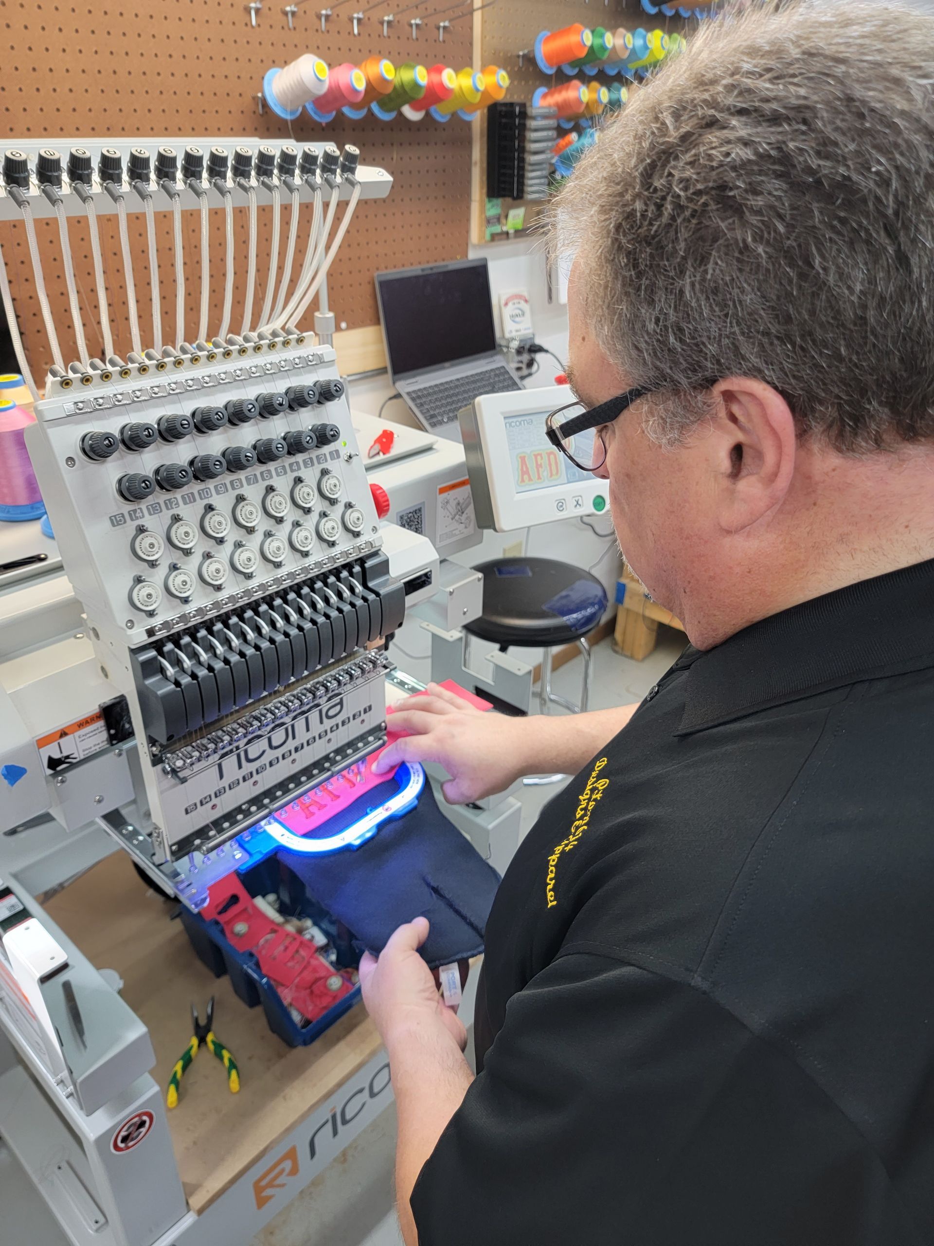 A man is working on an embroidery machine in a workshop.