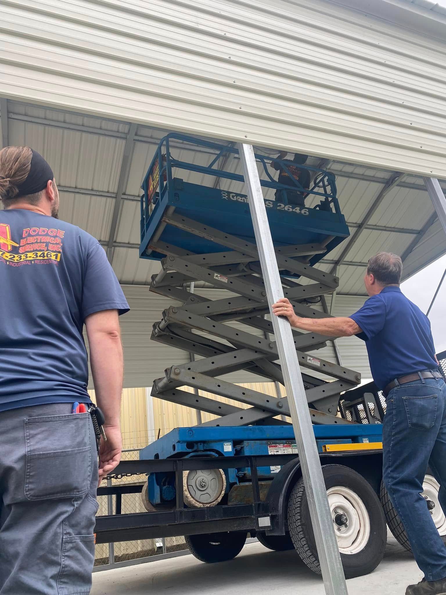 A group of men are working on a garage door with a scissor lift.