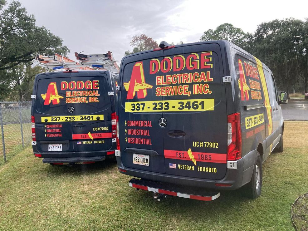 Two dodge electrical service vans are parked next to each other in a grassy field.