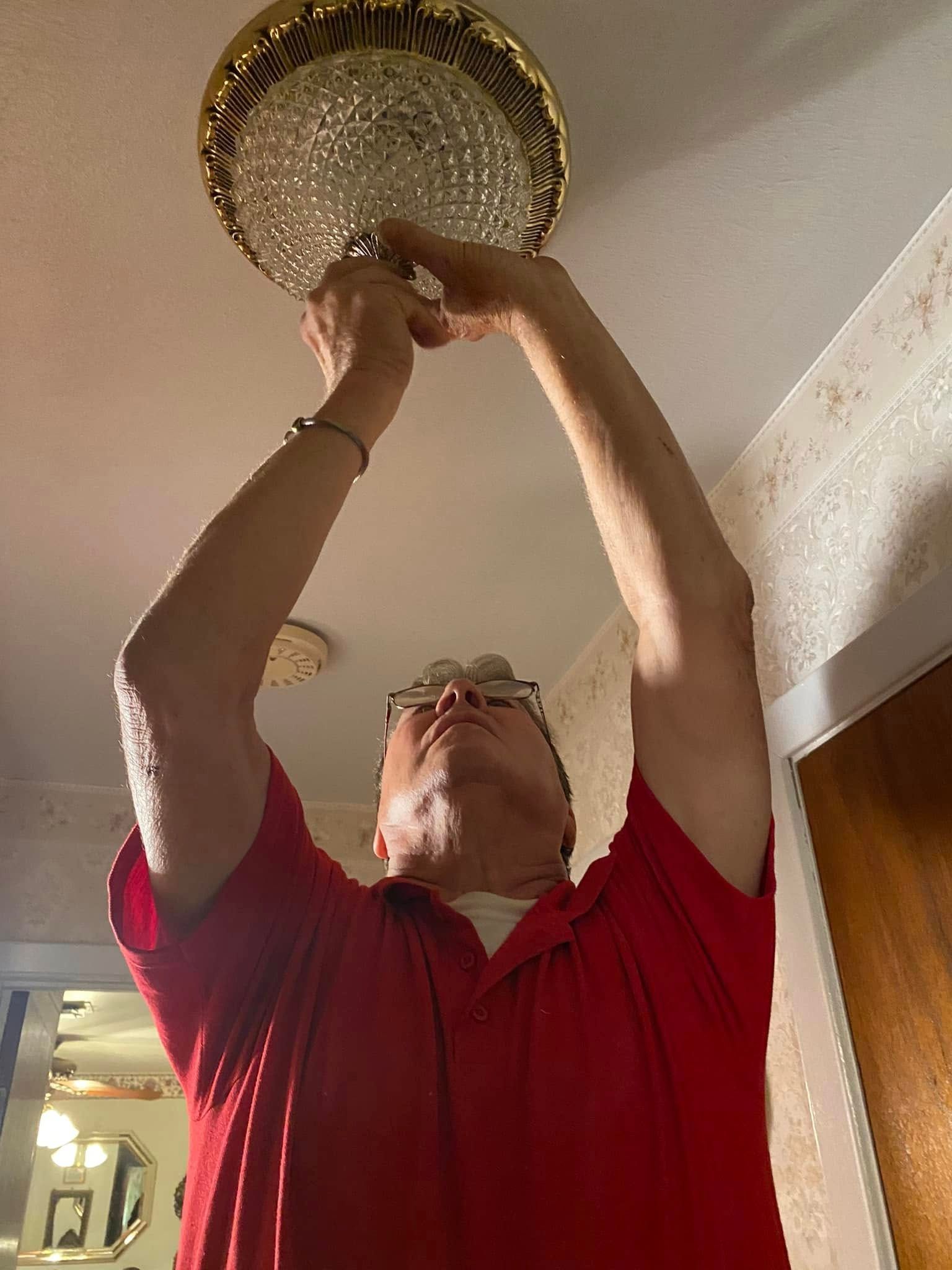 A man in a red shirt is fixing a ceiling light.