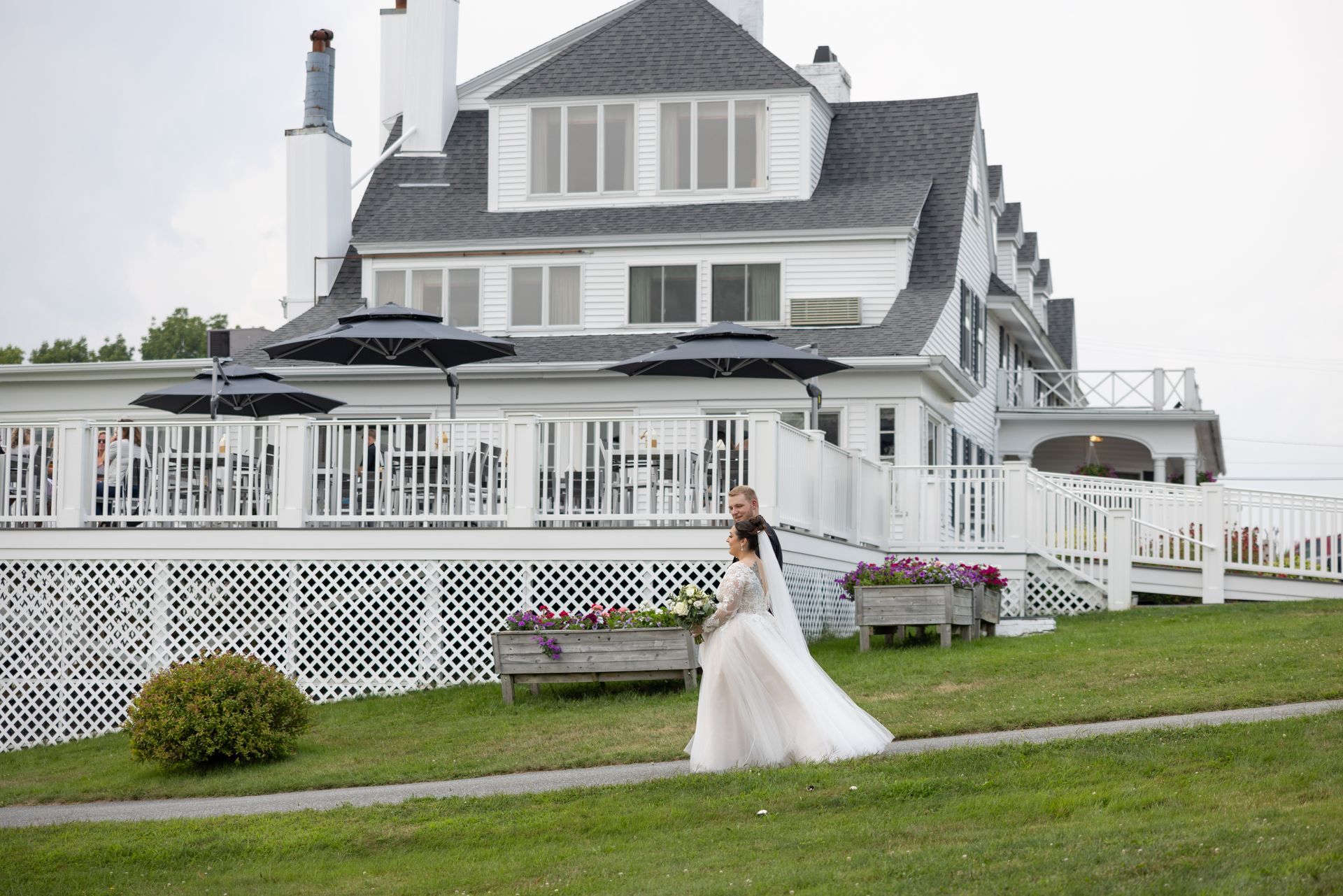 A bride and groom are walking in front of a large white house.