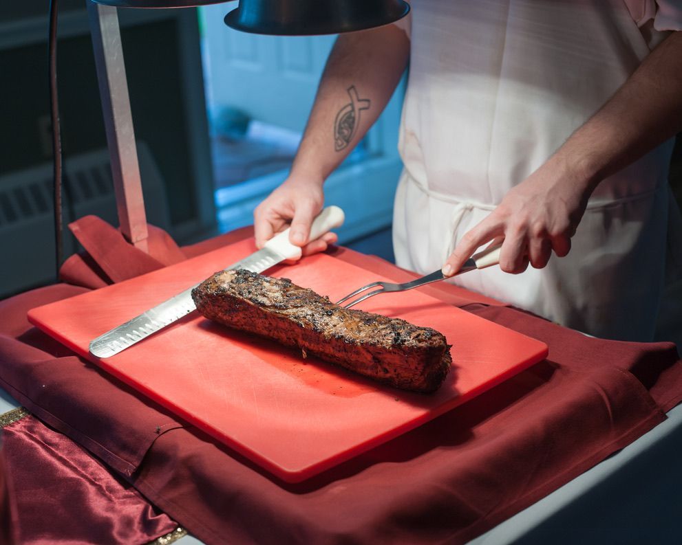 A man is cutting a piece of meat on a red cutting board.