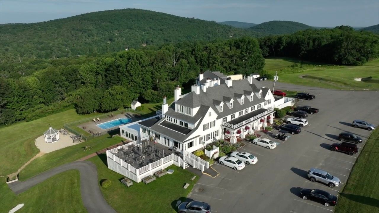 An aerial view of a large white house surrounded by trees and a parking lot.