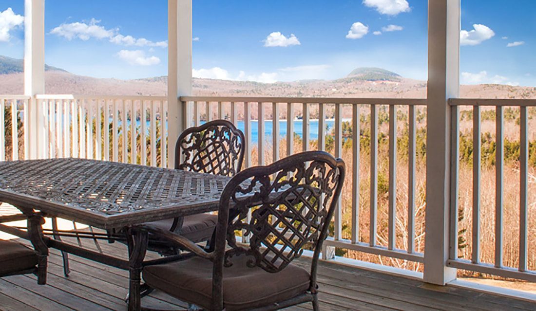 A porch with a table and chairs and a view of a lake.
