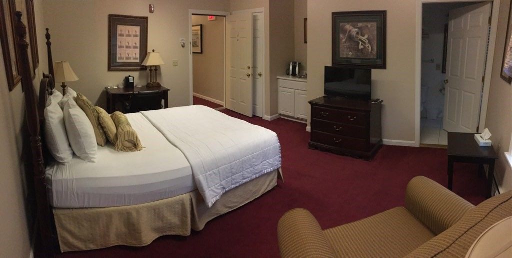 A hotel room with a king size bed , chair , television and dresser.