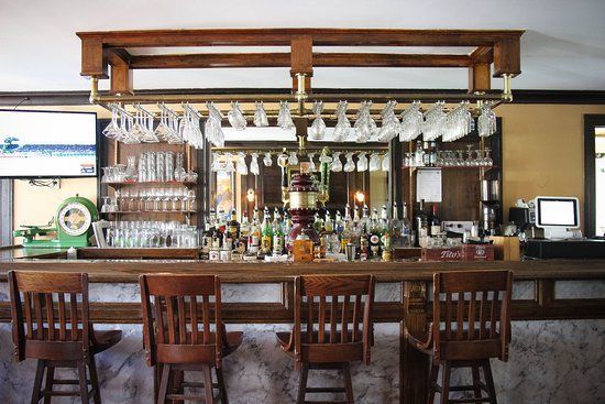 Bar with wooden stools, glassware, and liquor bottles. Mirrored back wall.