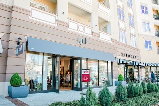 Exterior of a J.Jill store with open doors, next to a Sephora. Gray awnings, glass windows, and greenery.