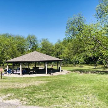 Park pavilion with people sitting at picnic tables on a sunny day.