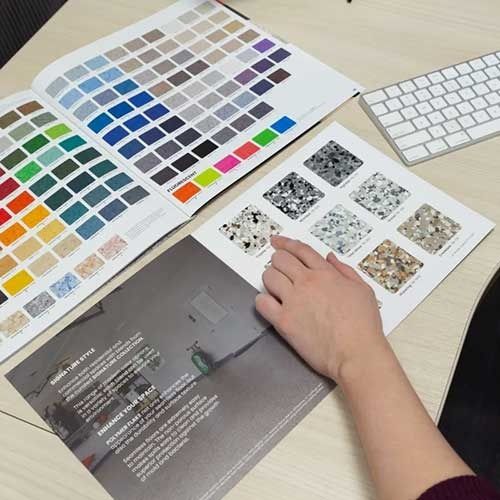 A person's hand points to a speckled flooring sample in a brochure with color swatches and a keyboard.