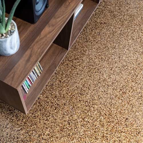 Brown wooden shelf with books and a plant on speckled brown flooring.
