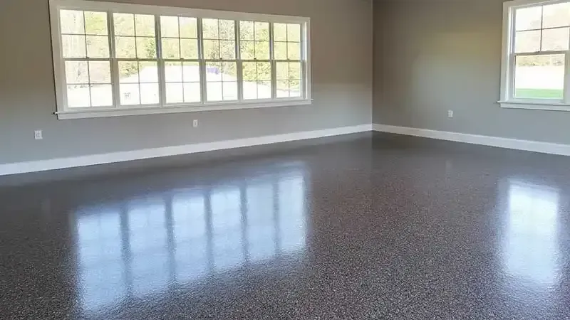 A room with gray walls, a shiny speckled gray floor, and two windows reflecting light.