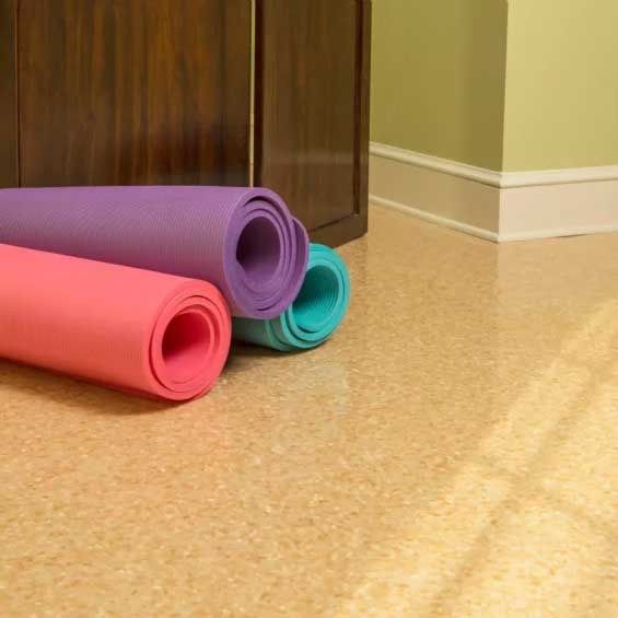Rolled yoga mats (pink, purple, teal) on a speckled beige floor, in front of a brown cabinet.