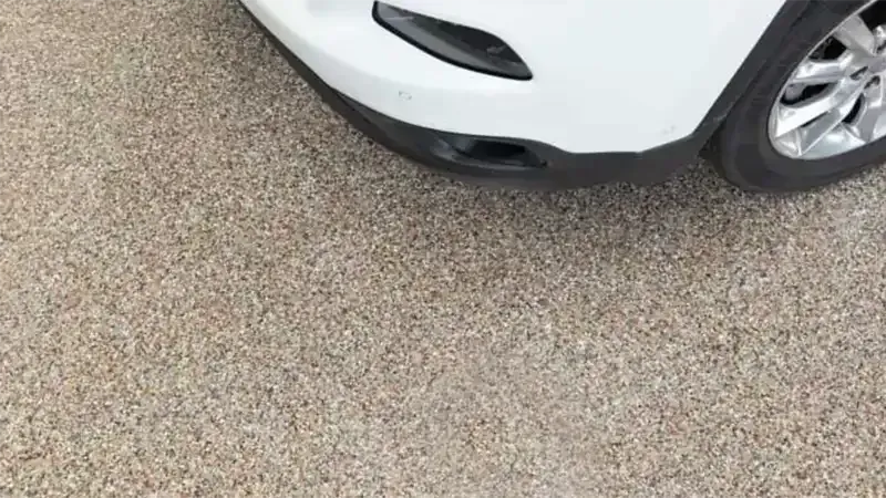 White car bumper, black grill, on a gravel surface.