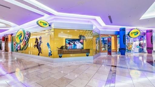 A Crayola Experience store in a mall with colorful murals and a TV screen.