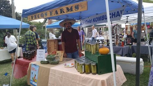 Man at Pecq Farms market stand, selling pickles and kombucha. Outdoor setting.