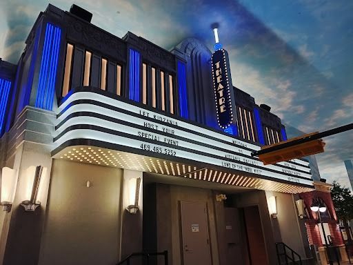 Art Deco theater facade with a marquee, lit blue and white, displaying show titles.