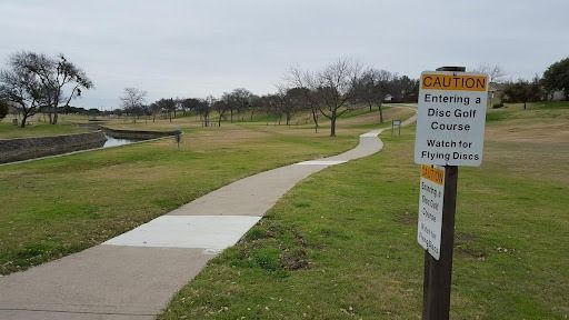 A pathway through a disc golf course with a warning sign.