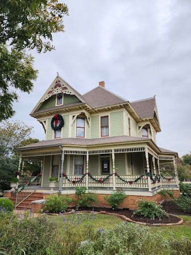 Victorian-style green house with holiday decorations on porch, under a cloudy sky.