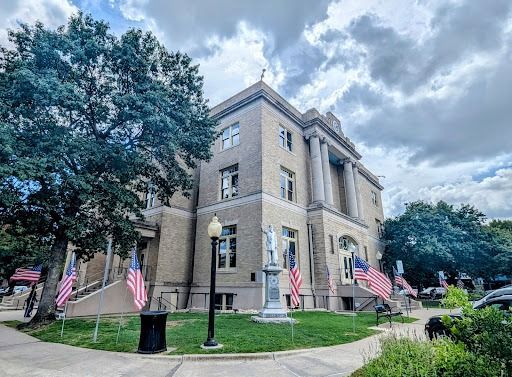Brick building with columns, flags, statues, and a cloudy sky in a park-like setting.