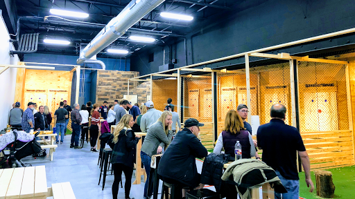 People socialize at an indoor axe-throwing venue with targets, wooden structures, and a casual atmosphere.