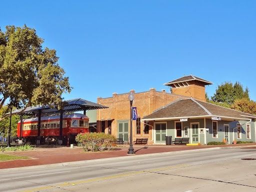 Train depot with red train car, brick building, and green building under a clear blue sky.
