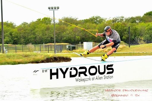 Wakeboarder at Hydrous Wake Park in Allen Station, TX. He is in mid-air, giving a thumbs up.