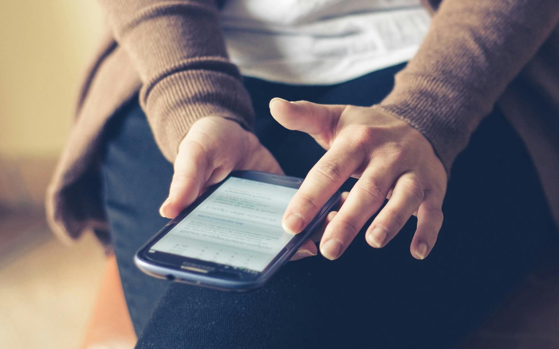 Person holding a smartphone, tapping the screen with their finger. Focus on the hands and phone.
